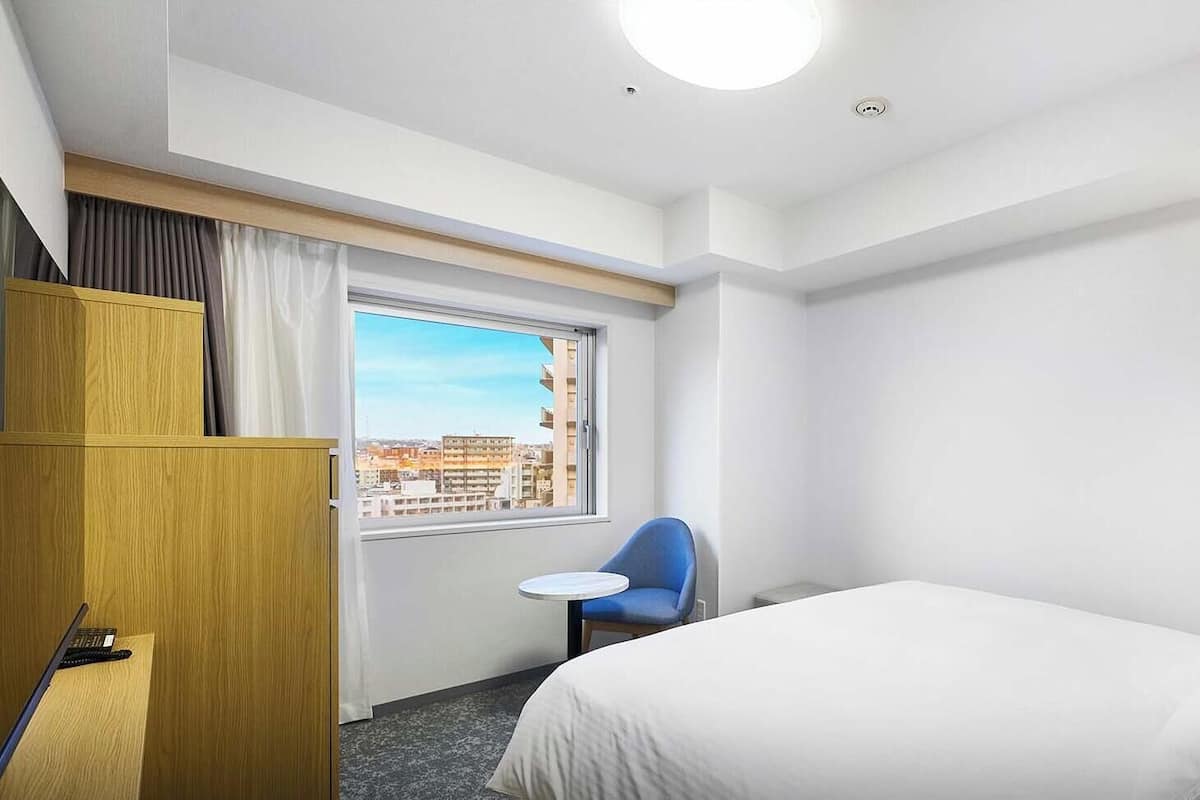 Habitación de hotel con cama, escritorio, silla y ventana con vista a la ciudad.
