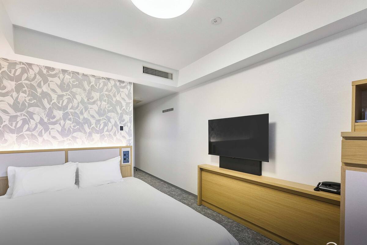 A hotel room with a large bed, a flat-screen TV mounted on a wooden dresser, and a patterned wall.
