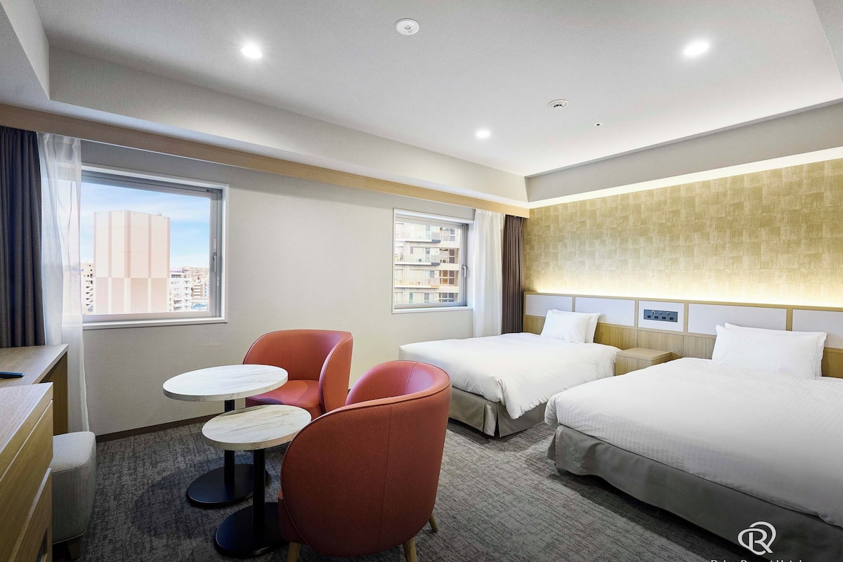 A hotel room with two beds, a desk, a chair, and a small table.