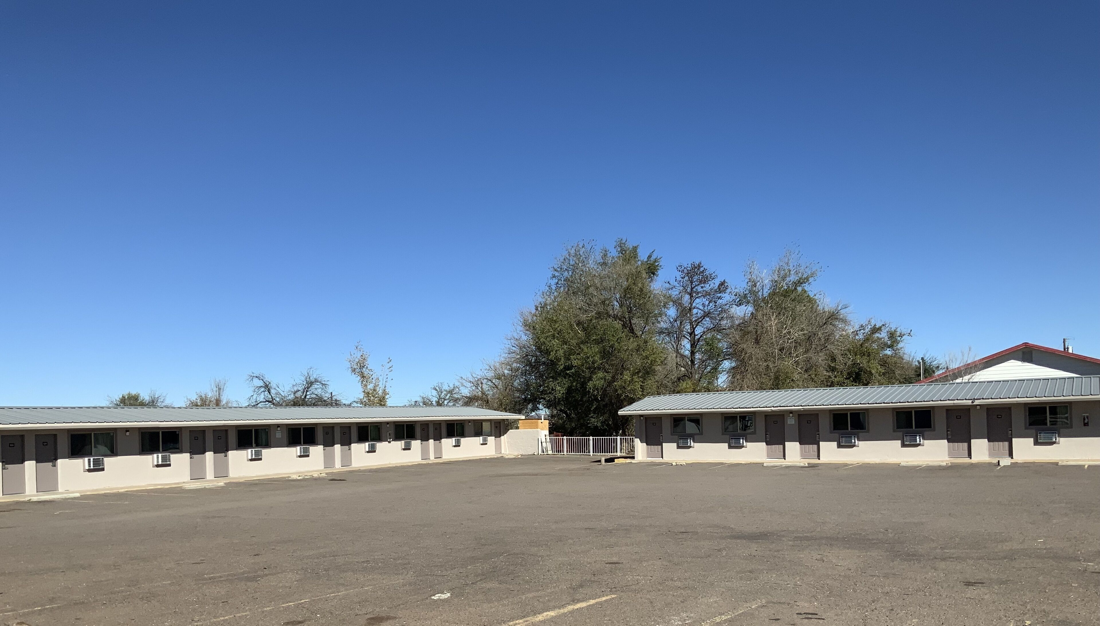 A motel with multiple rooms, a parking lot, and trees in the background.