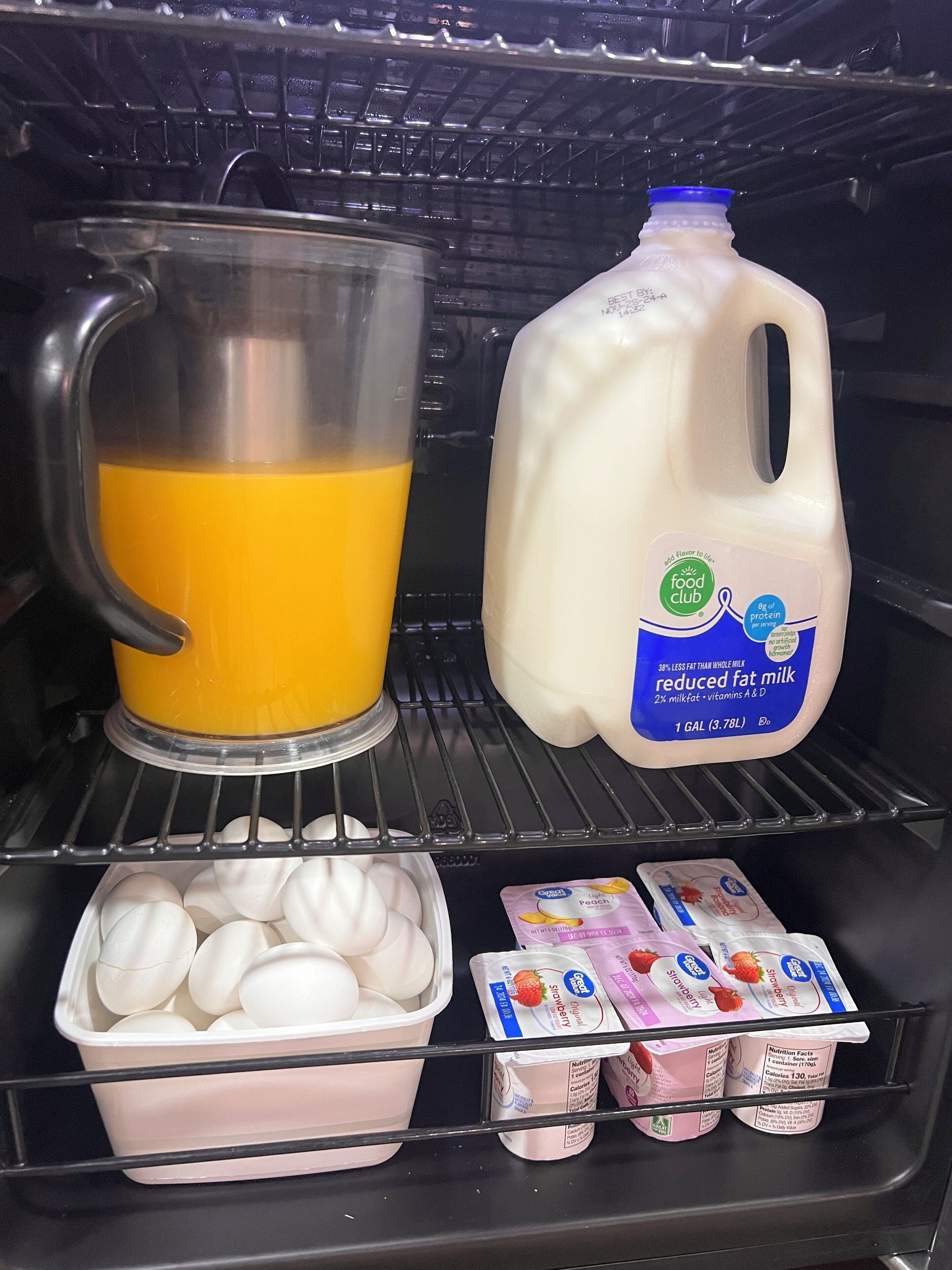 A refrigerator containing a carton of reduced fat milk, a jug of orange juice, a container of eggs, and several packets of strawberry yogurt.