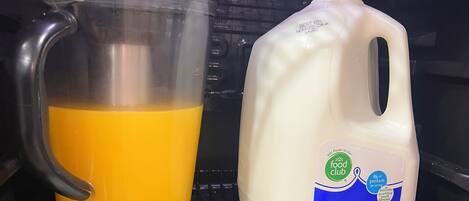 A refrigerator containing a carton of reduced fat milk, a jug of orange juice, a container of eggs, and several packets of strawberry yogurt.