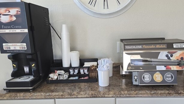 A coffee station with a coffee machine, a touchless pancake maker, and a cup dispenser. - Value Lodge (Alpine)