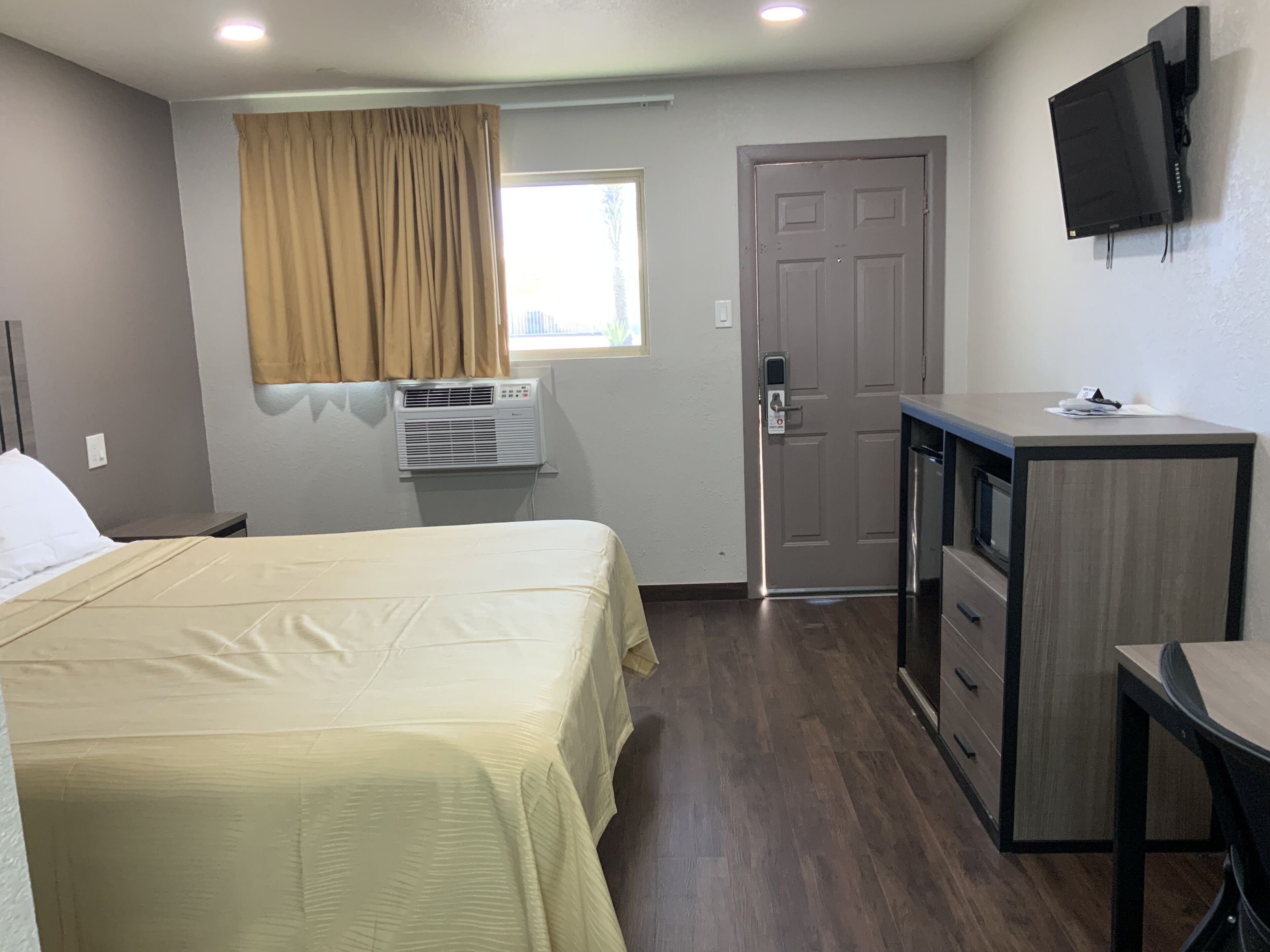 Una habitación de hotel compacta con cama, escritorio, silla, televisión y aire acondicionado.
