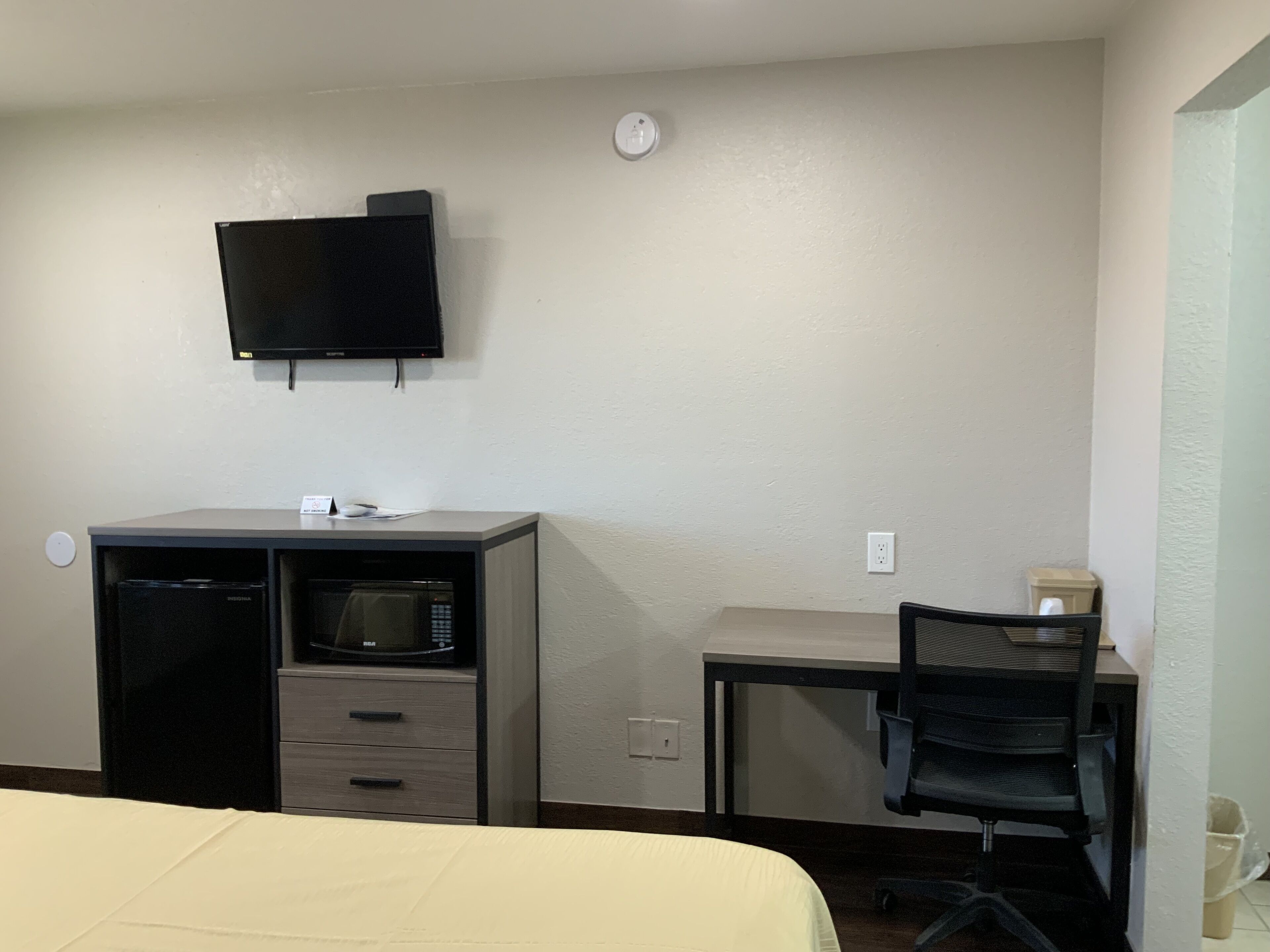 A hotel room with a bed, a desk with a computer, a microwave, and a TV mounted on the wall.