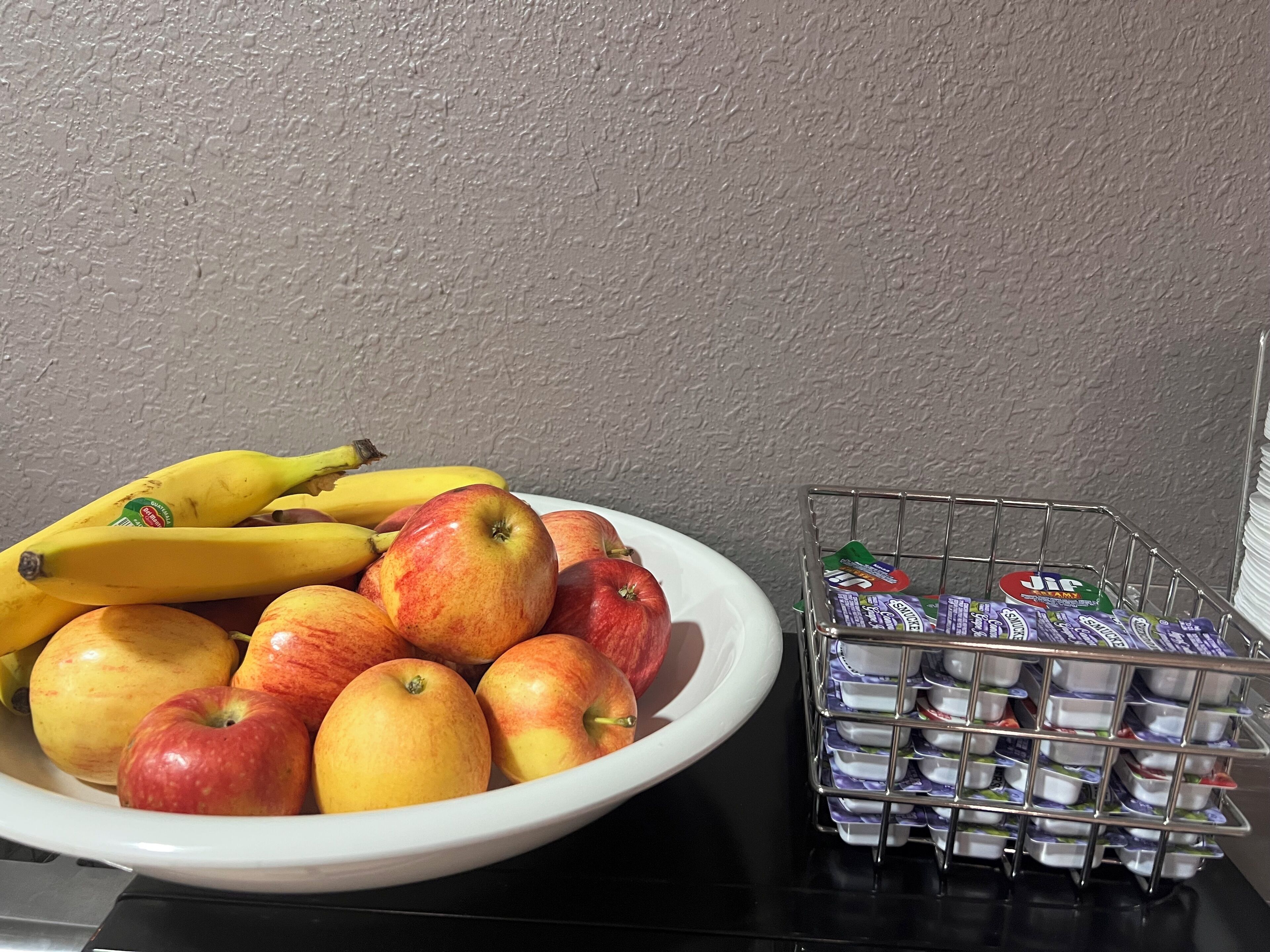A bowl of fruits including bananas and apples, and a metal basket with yogurt containers.