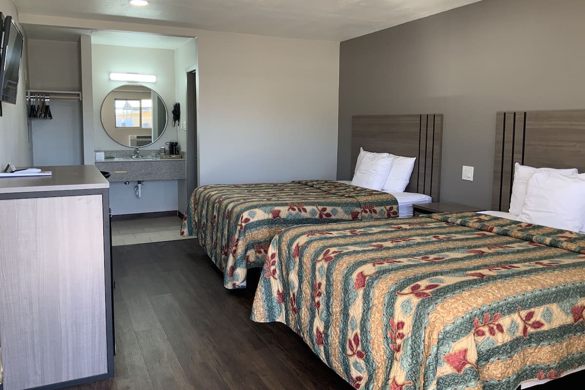 A hotel room with two beds, a desk, a mirror, and a bathroom visible through an open door.