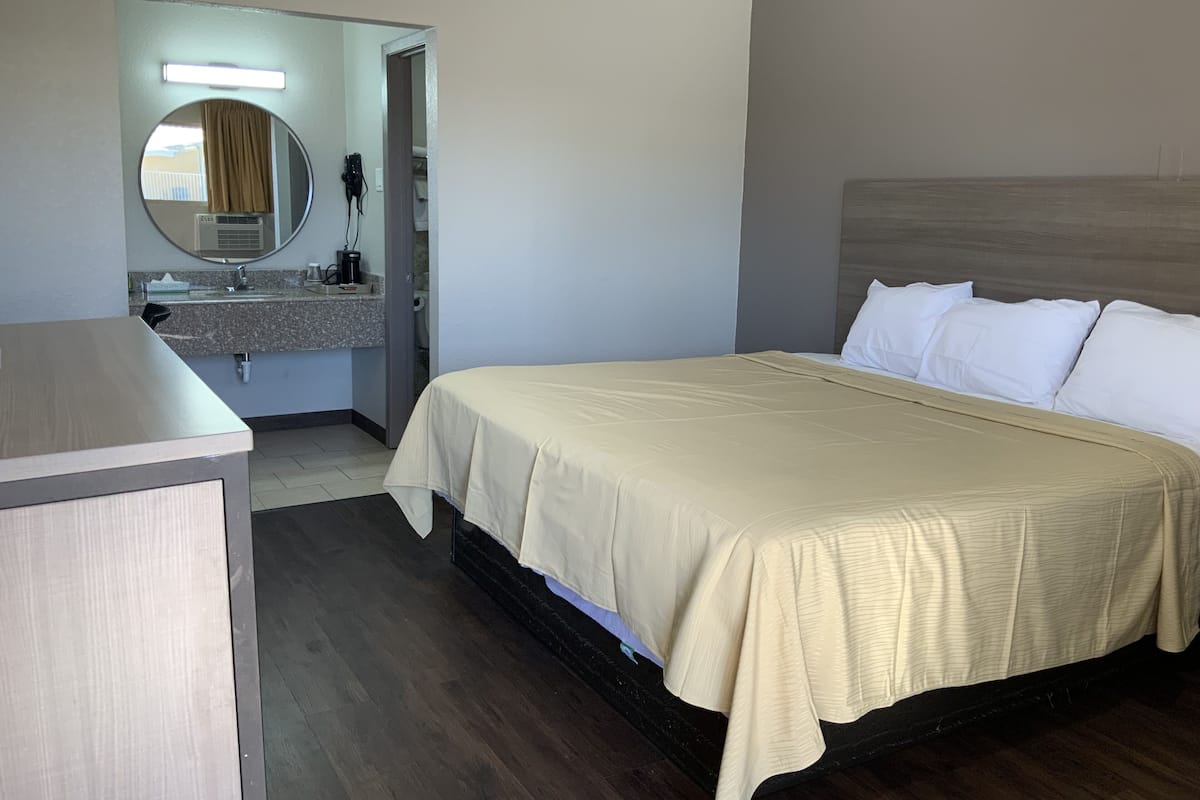 A hotel room with a bed, a bedside table, a mirror, and a bathroom with a sink and towel rack.