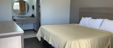 A hotel room with a bed, a bedside table, a mirror, and a bathroom with a sink and towel rack.