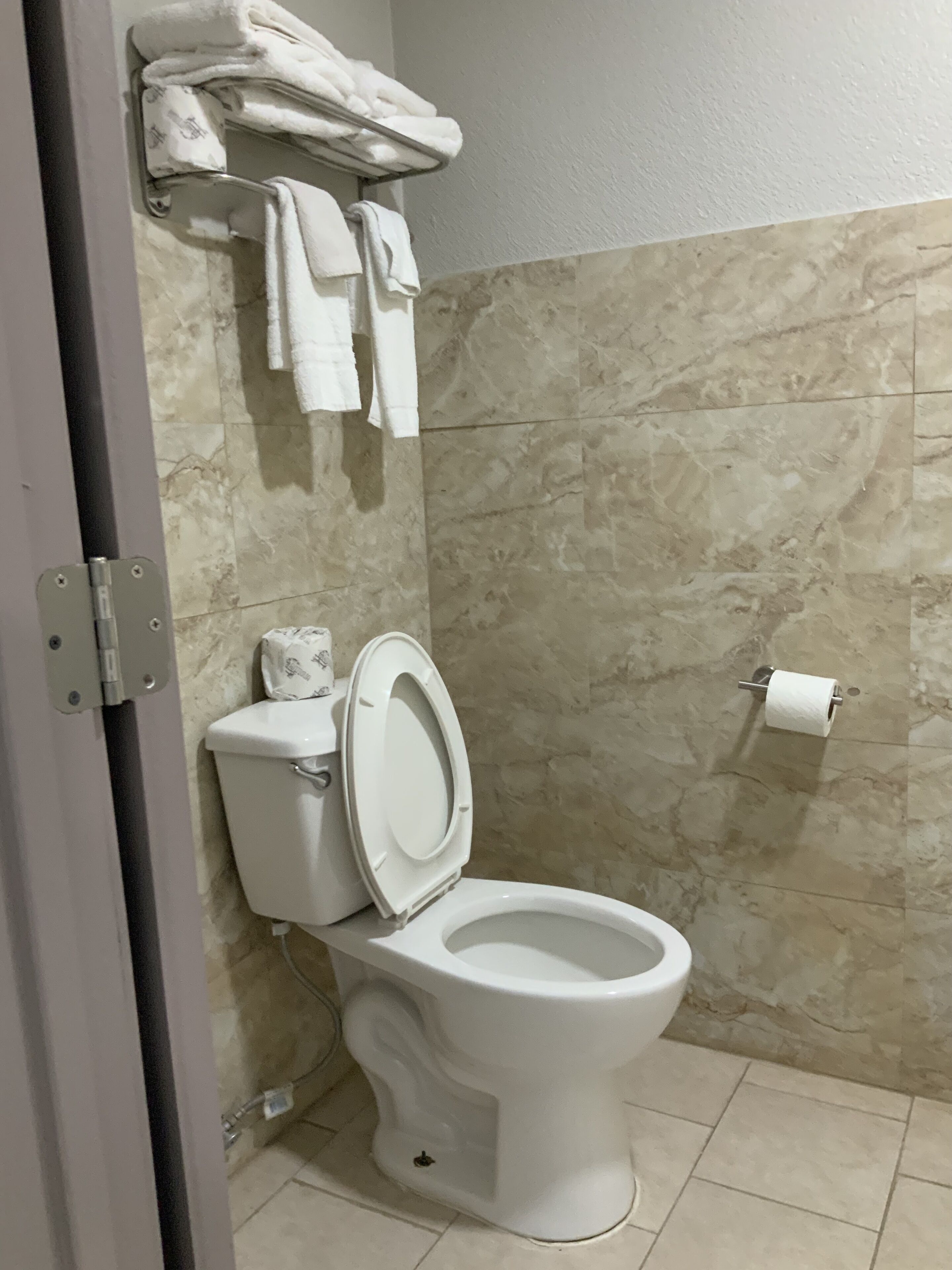 Une salle de bain avec des toilettes blanches, des murs en marbre et un porte-serviettes avec des serviettes pliées.