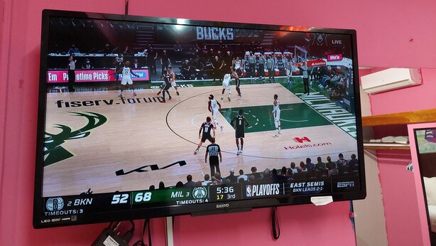 Ein Basketballspiel auf einem großen Fernsehbildschirm, der an einer rosafarbenen Wand angebracht ist.