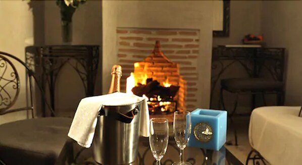 A room with a fireplace, a table with a champagne bucket, glasses, and a blue decorative item.