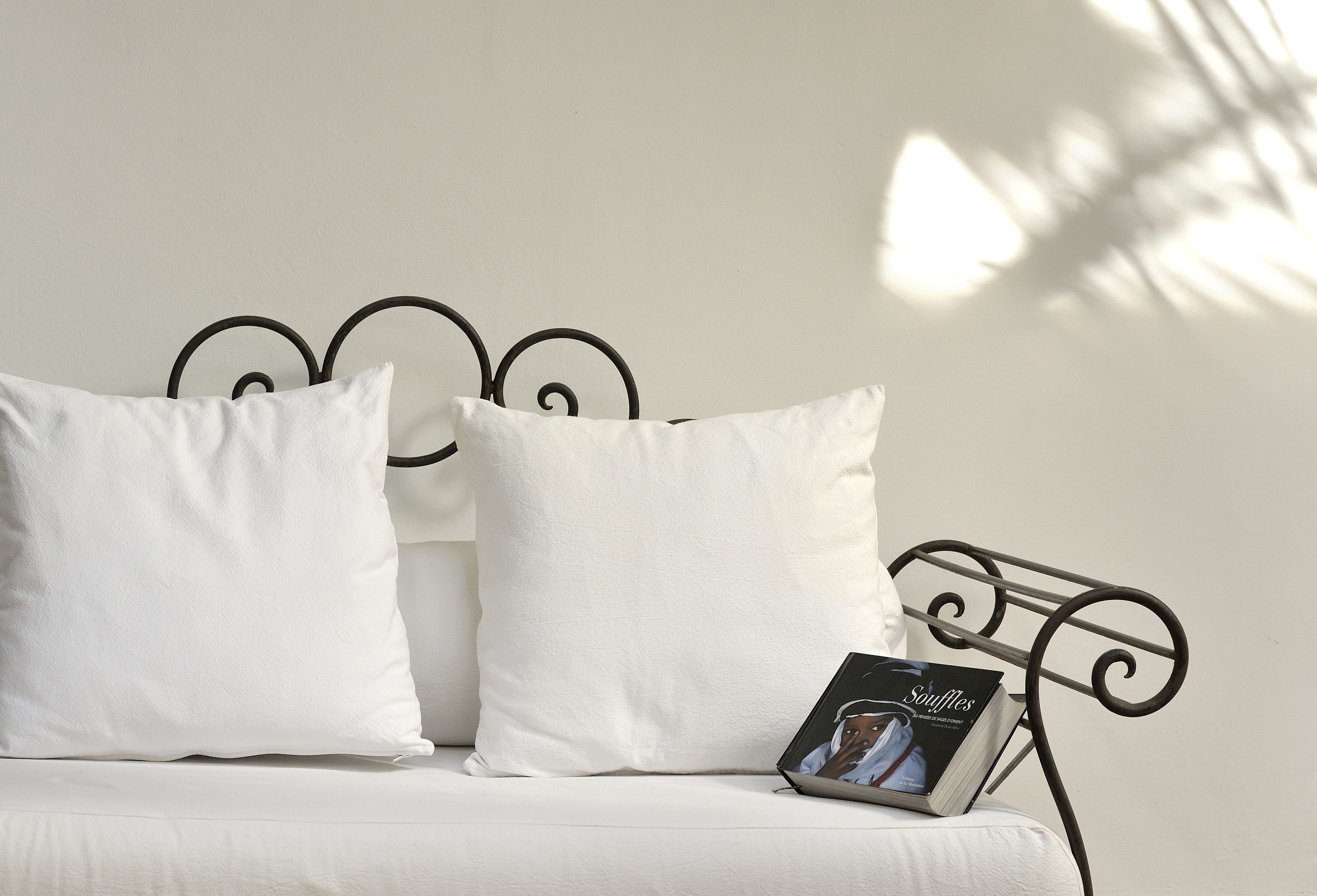 A bed with white bedding and a metal headboard. A book titled 'Souffles' is placed on the bed.
