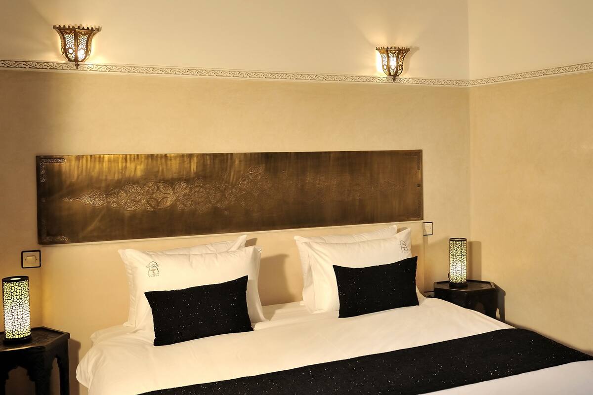 Une chambre d’hôtel avec un grand lit, deux tables de chevet avec des lampes, une tête de lit décorative et un miroir dans un coin.