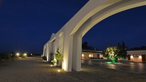 Un edificio con una amplia entrada arqueada, un camino de acceso pavimentado e iluminación exterior.