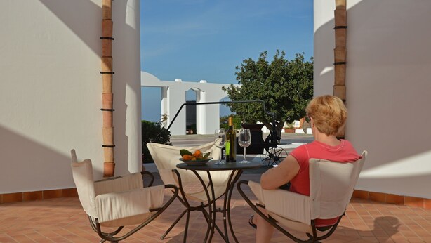Une personne est assise à une table, devant laquelle on aperçoit une structure blanche et, au loin, un arbre.