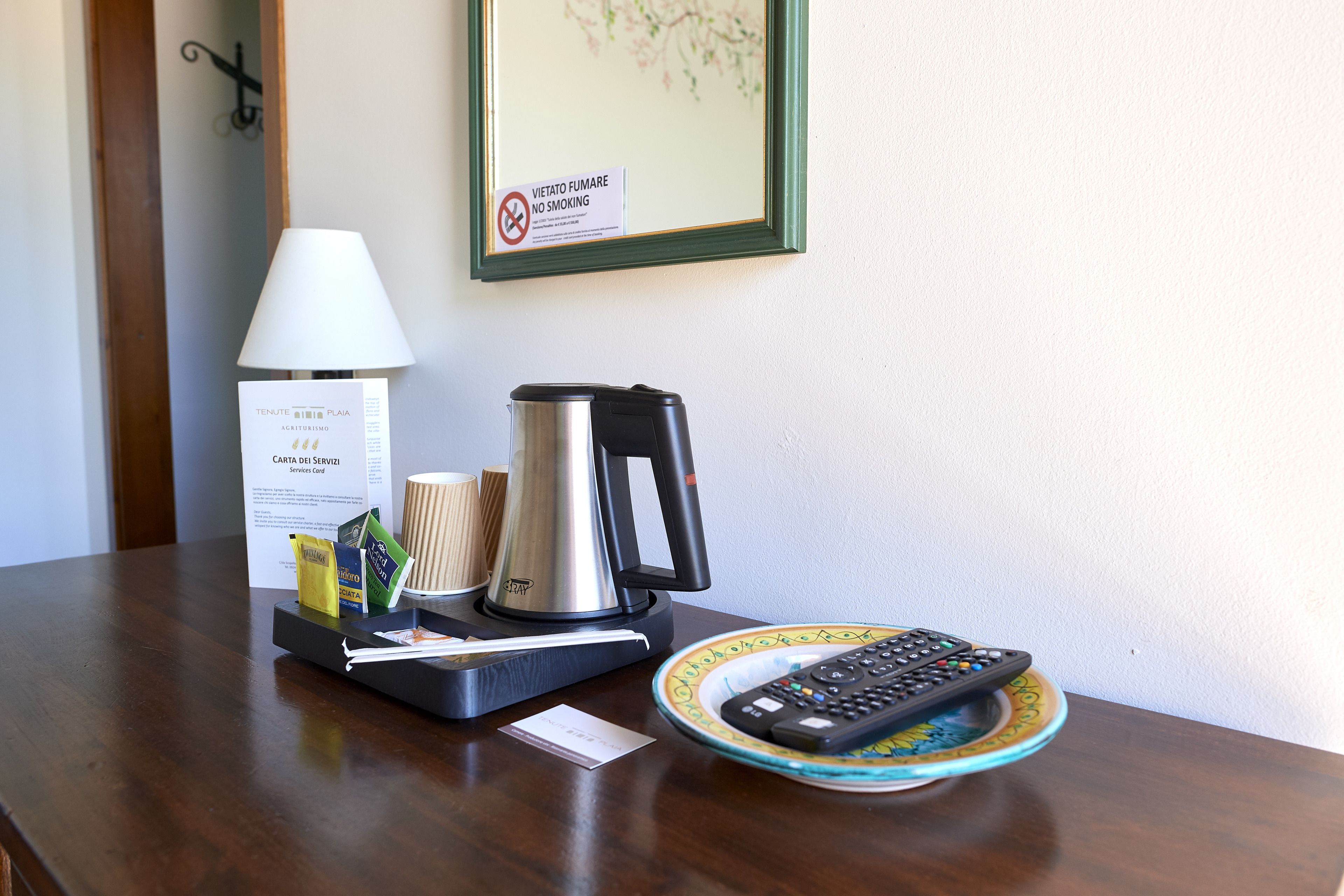 A hotel room table with a lamp, a coffee pot, a remote control, and a menu.
