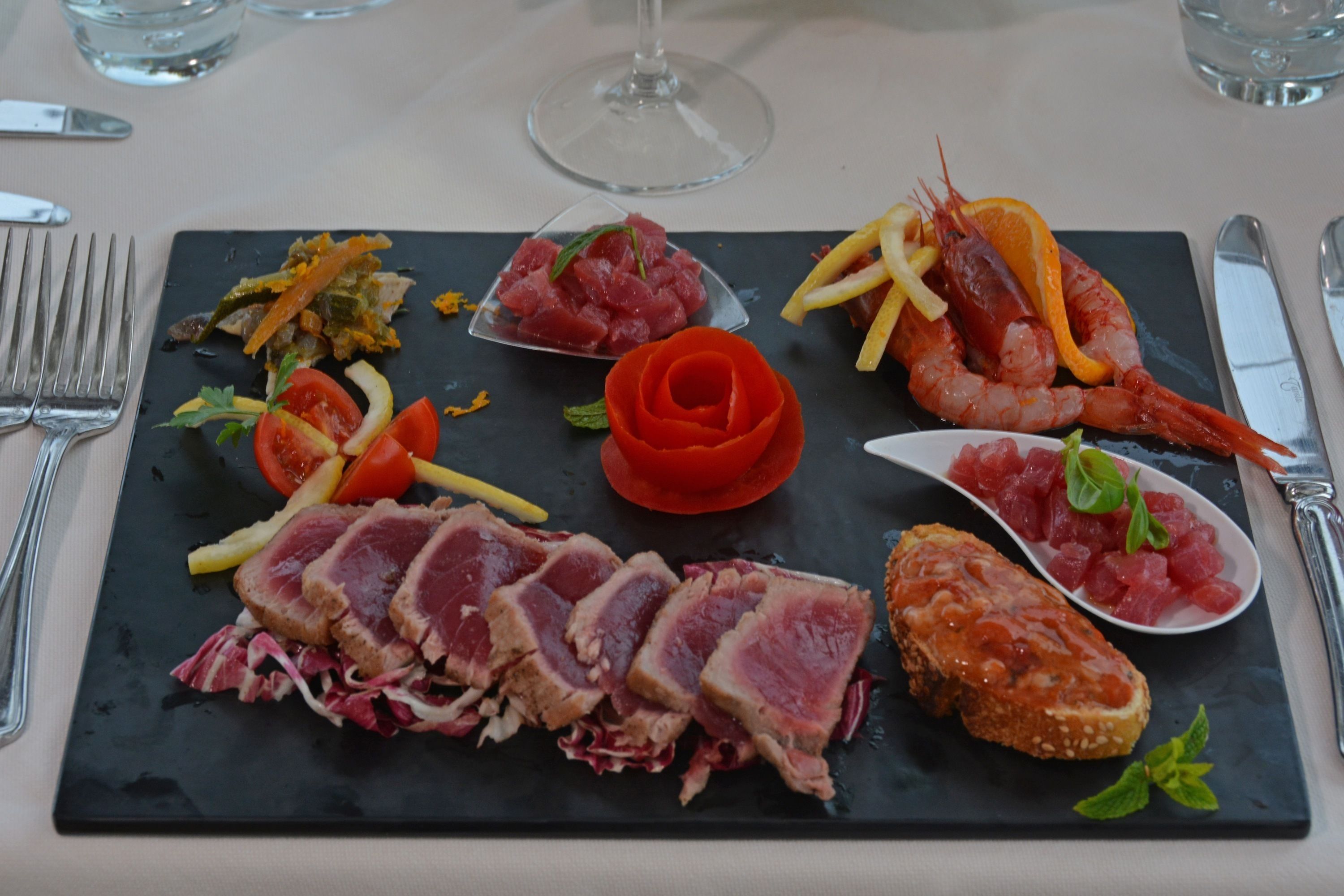 Un tagliere in ardesia nera con diversi cibi, tra cui bistecca, gamberi e verdure.