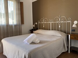 A neatly made bed with a patterned bedspread and two pillows, a bedside table with a lamp, and a window with curtains.