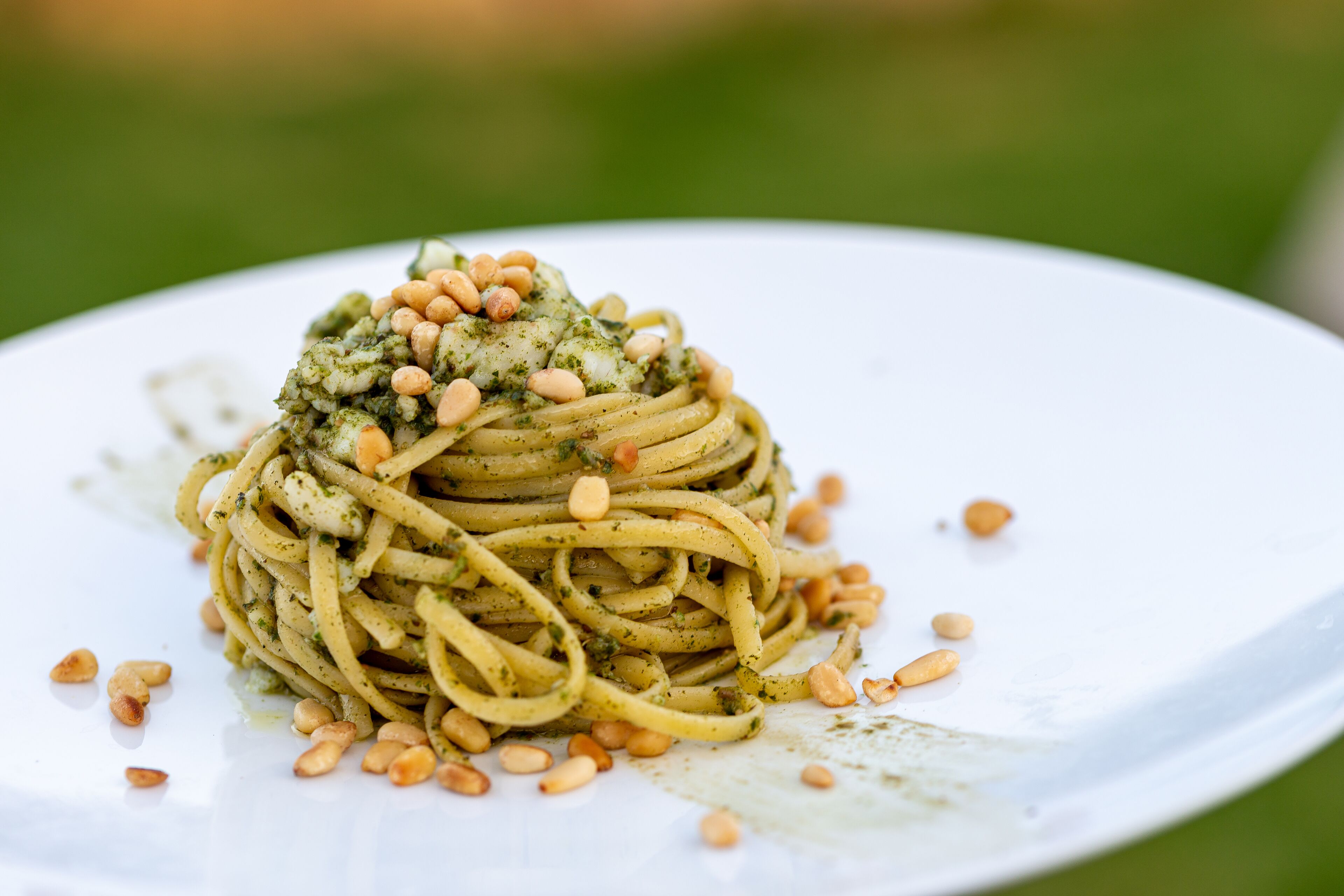 A plate of spaghetti with pesto and pine nuts.