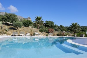 Una piscina azul cristalina con sillones de descanso y palmeras al fondo.