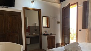 Una habitación de hotel con una cama, una silla, un escritorio, un espejo y una ducha.