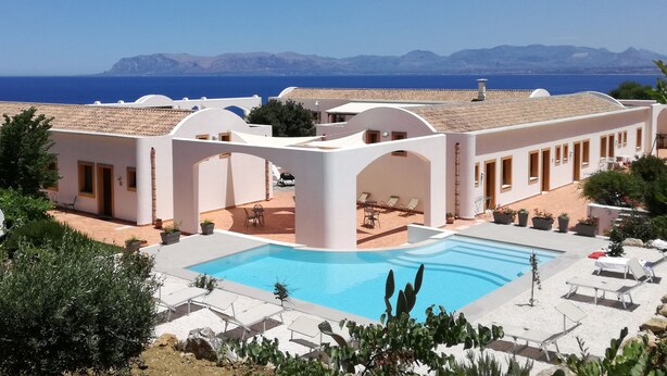 Un resort con piscina, mobiliario exterior y vista al mar.