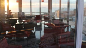 A modern lounge with a glass wall offering a view of the sea and buildings.