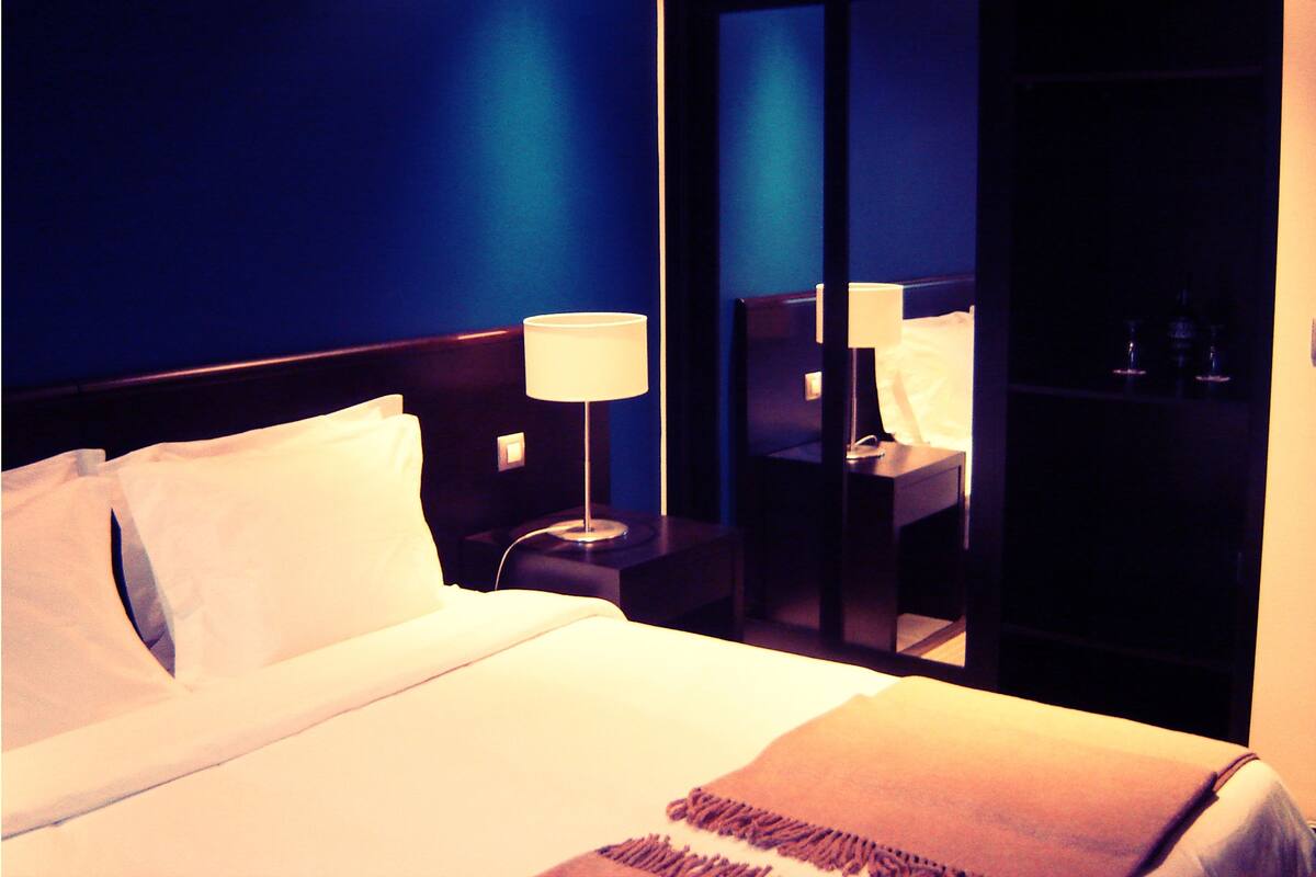 A hotel room with a bed, a nightstand, a lamp, and a mirror.
