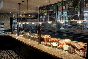 A buffet counter with various meats, vegetables, and bread.