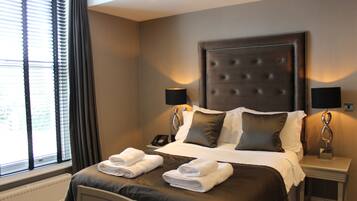 Habitación de hotel con una cama grande, dos lámparas de noche, una mesita de noche con teléfono y una ventana con persianas.