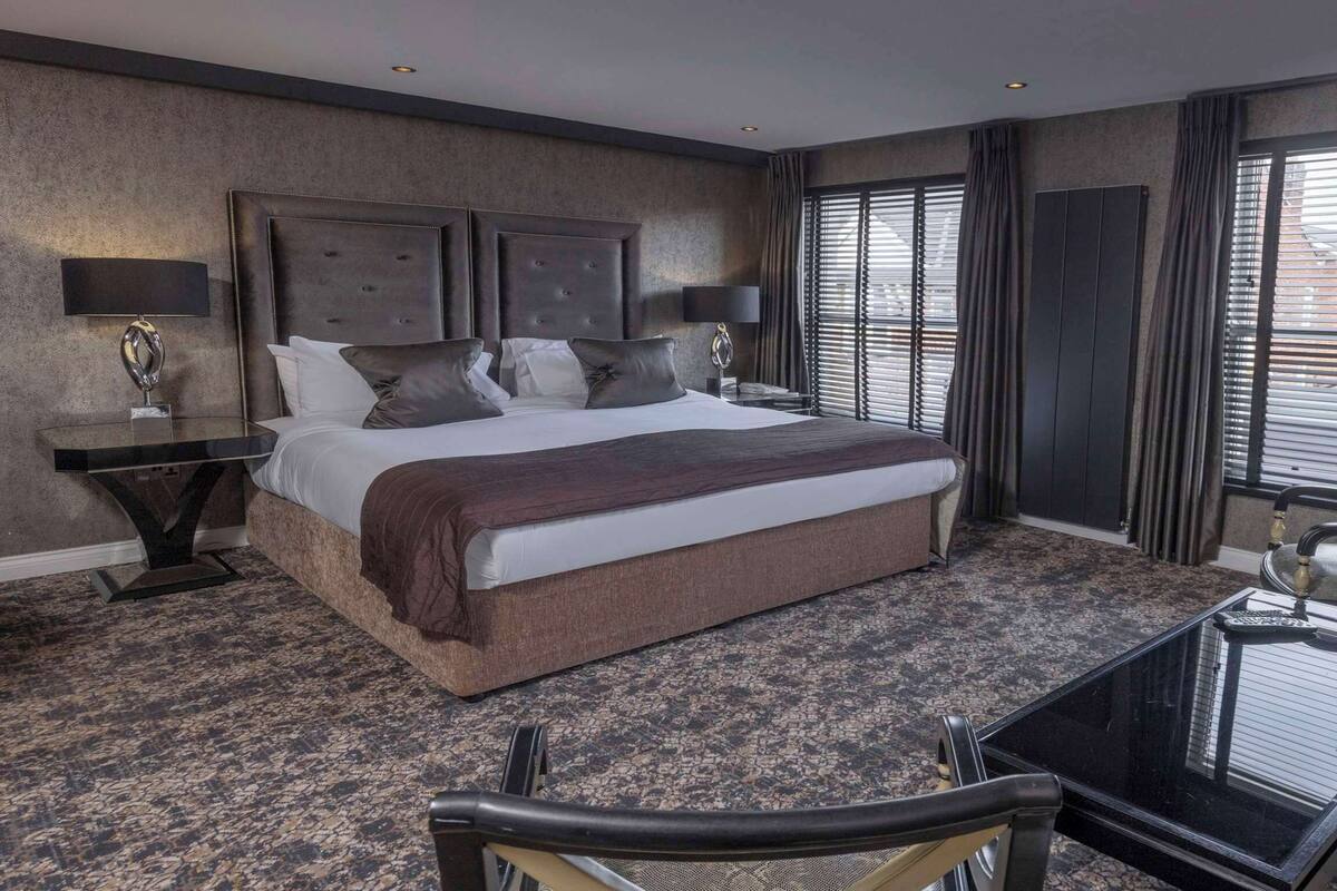 A hotel room with a large bed, a glass coffee table, a seating area, and a view of the city through large windows.