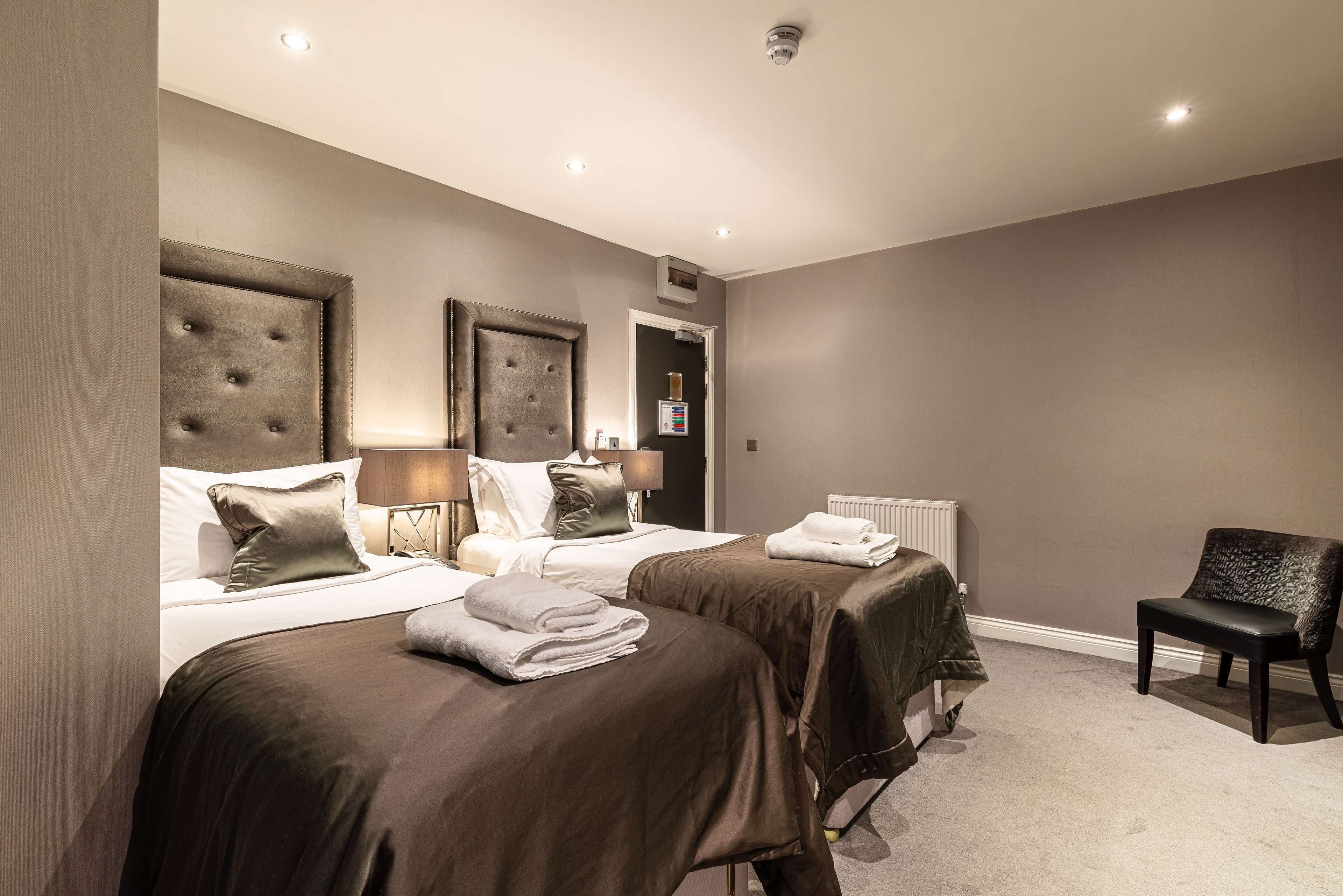 A hotel room with two beds, a chair, and a radiator.