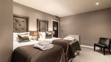 A hotel room with two beds, a chair, and a radiator.