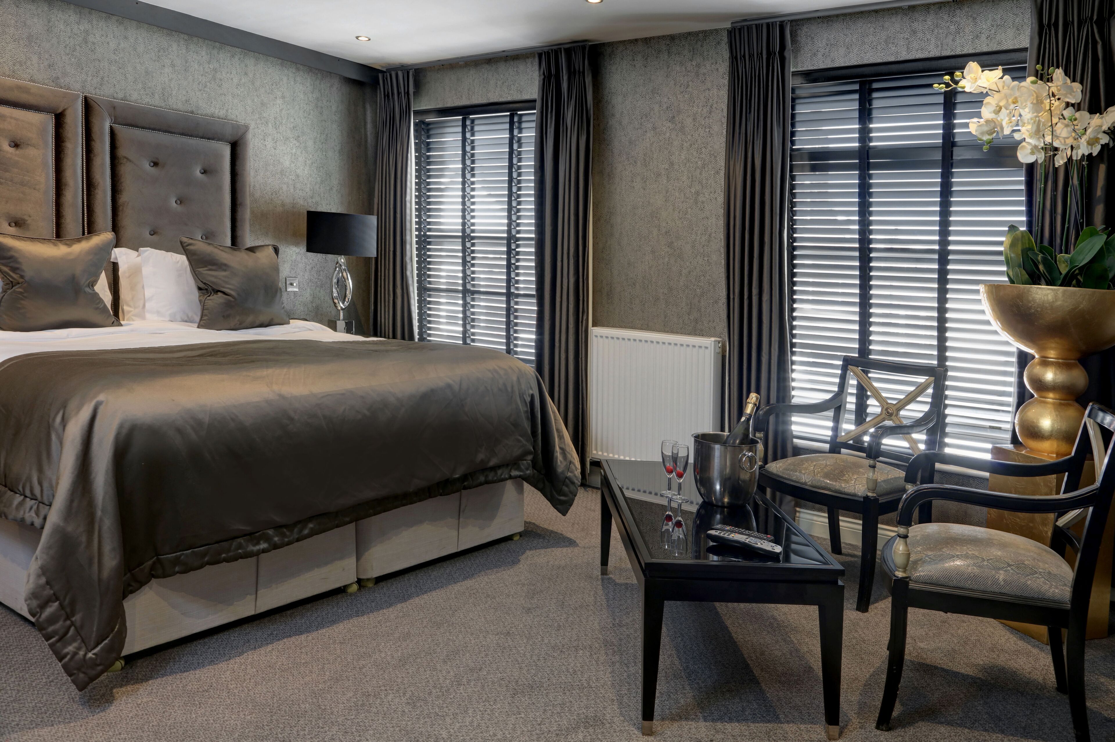 A modern hotel room with a large bed, a sitting area with a table and chairs, and a view through the window.