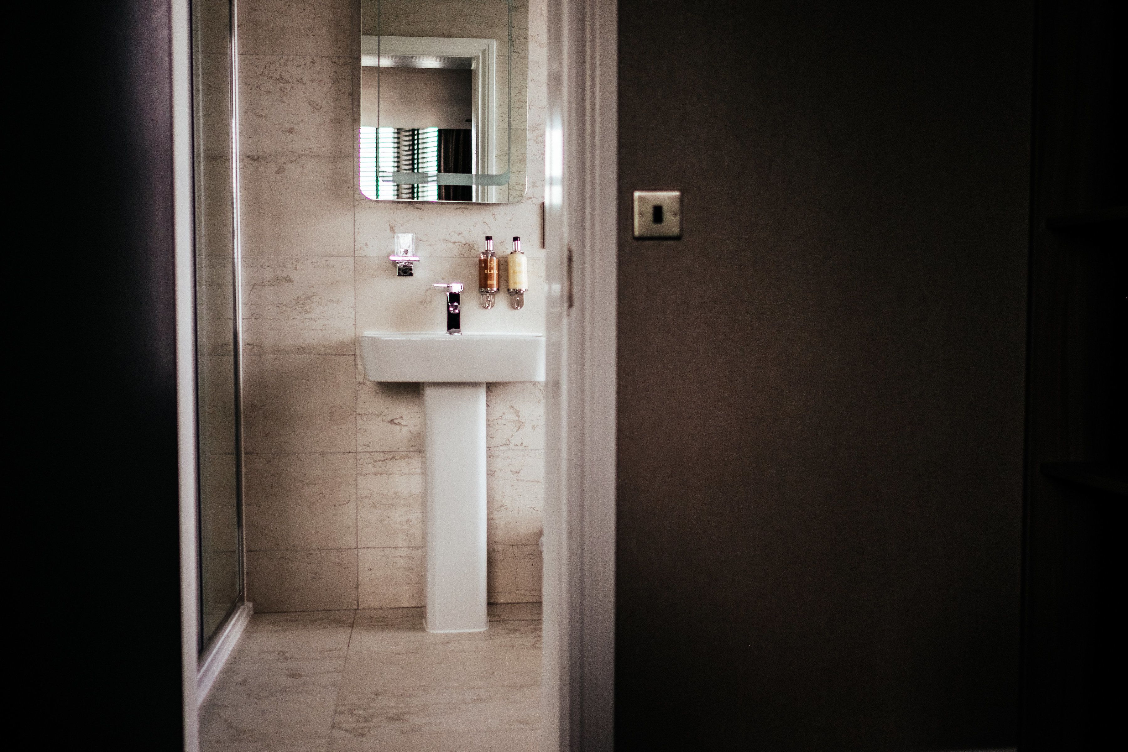 A modern bathroom with a white pedestal sink, a mirror above it, and toiletries on the sink.