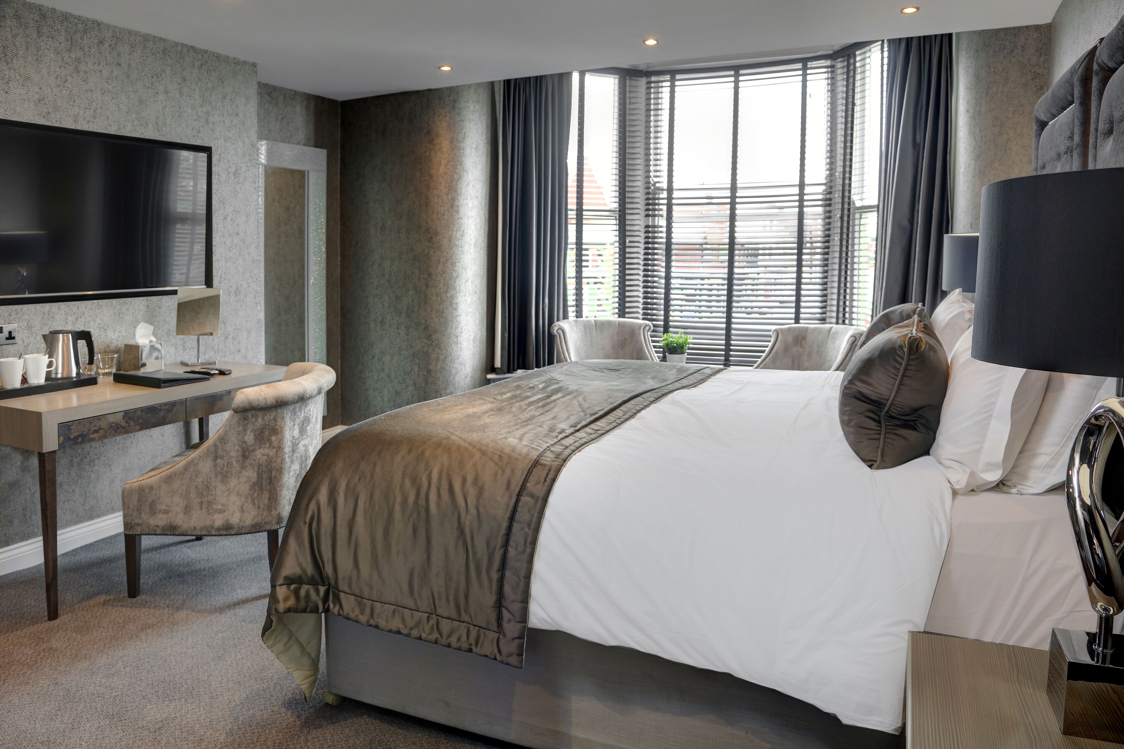 A modern hotel room with a large bed, a desk with a chair, a television, and a window with curtains.