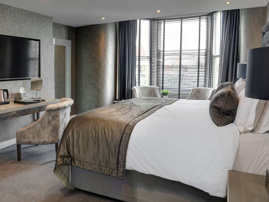 A modern hotel room with a large bed, a desk with a chair, a television, and a window with curtains.