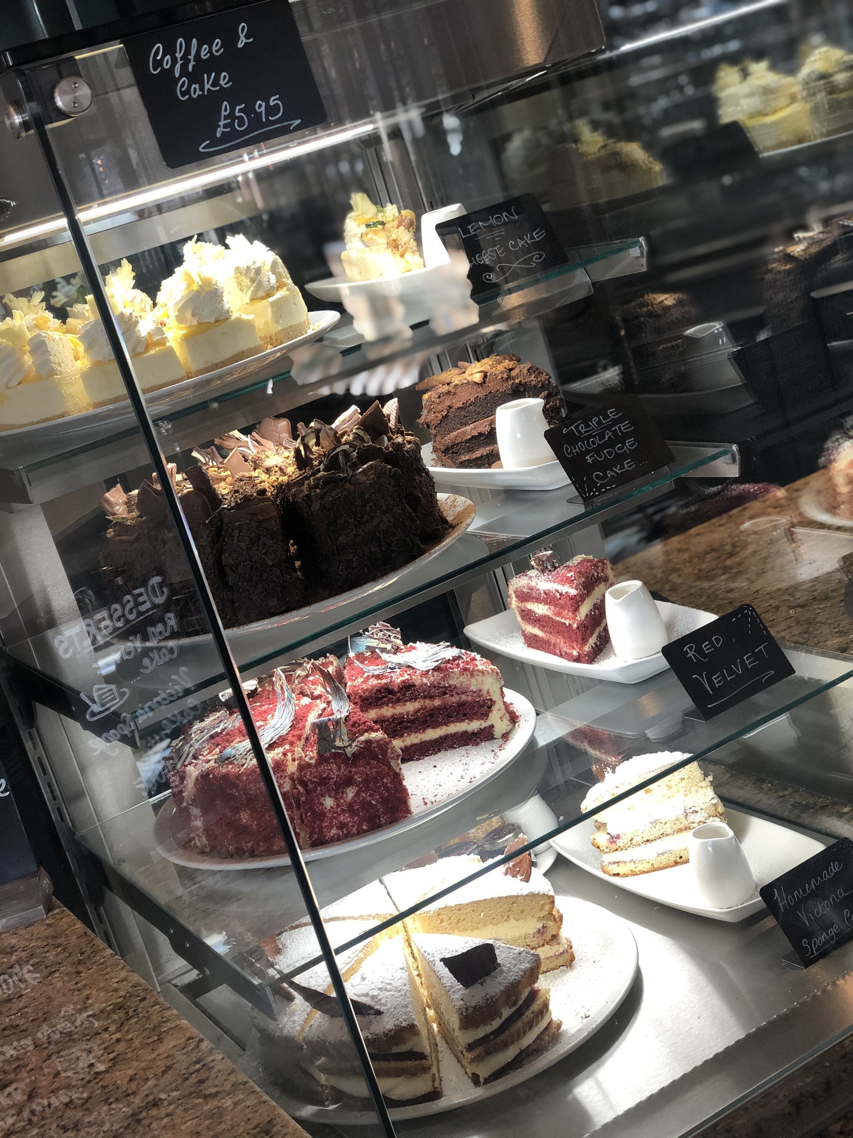 A dessert display case with various cakes and pastries, including a lemon cake, triple chocolate fudge cake, and red velvet cake.