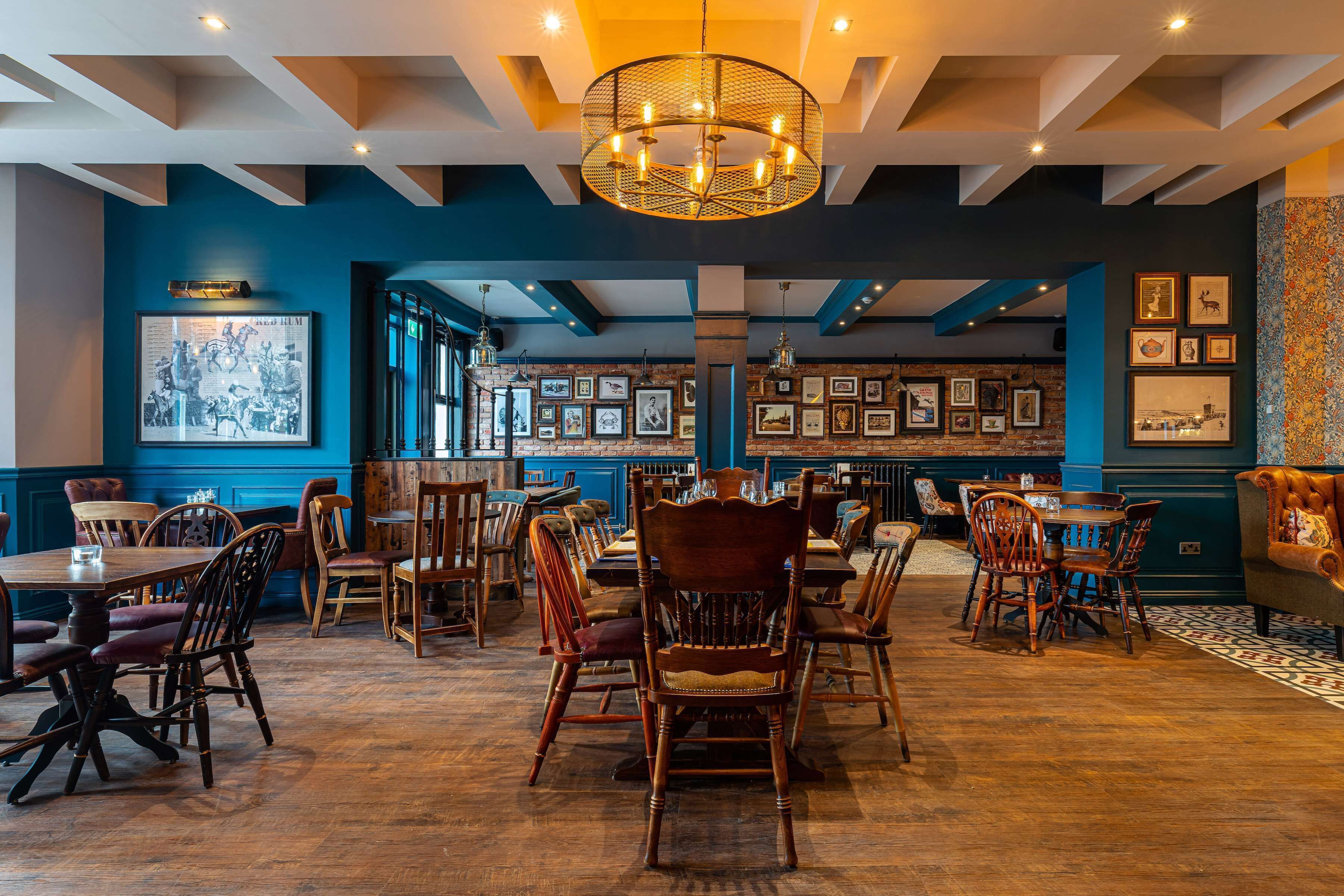 A restaurant with wooden tables and chairs, a large chandelier, and framed pictures on the walls.