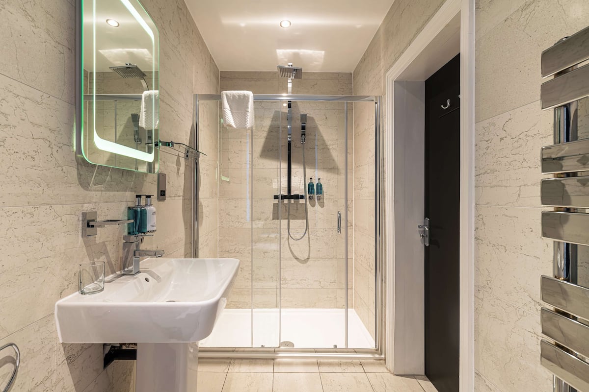 A modern bathroom with a glass-enclosed shower, a white sink, and a mirror with a lighted frame.