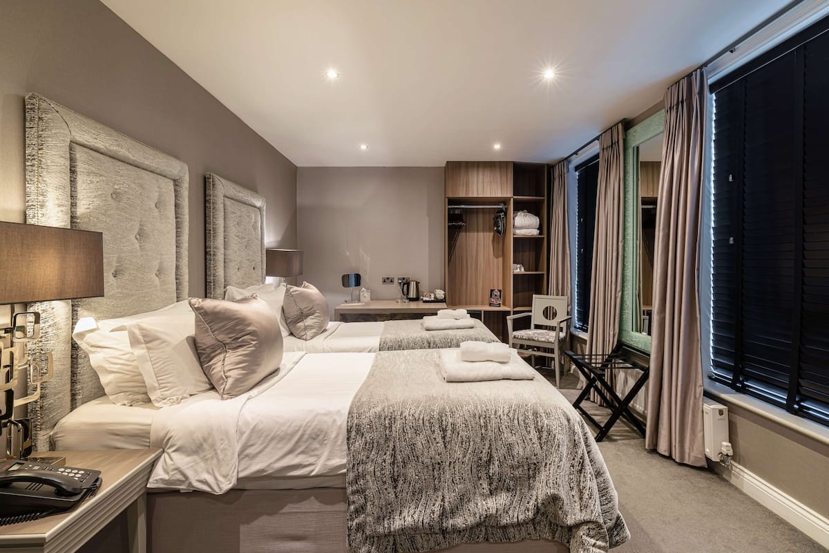 A hotel room with two beds, a desk, a wardrobe, and a large window with curtains.