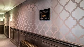 Un pasillo de hotel con un papel tapiz estampado, un cartel que indica que las habitaciones están disponibles y un radiador.