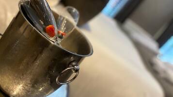 A metallic bucket with a bottle of champagne and a small orange object inside, placed on a surface near a couch.