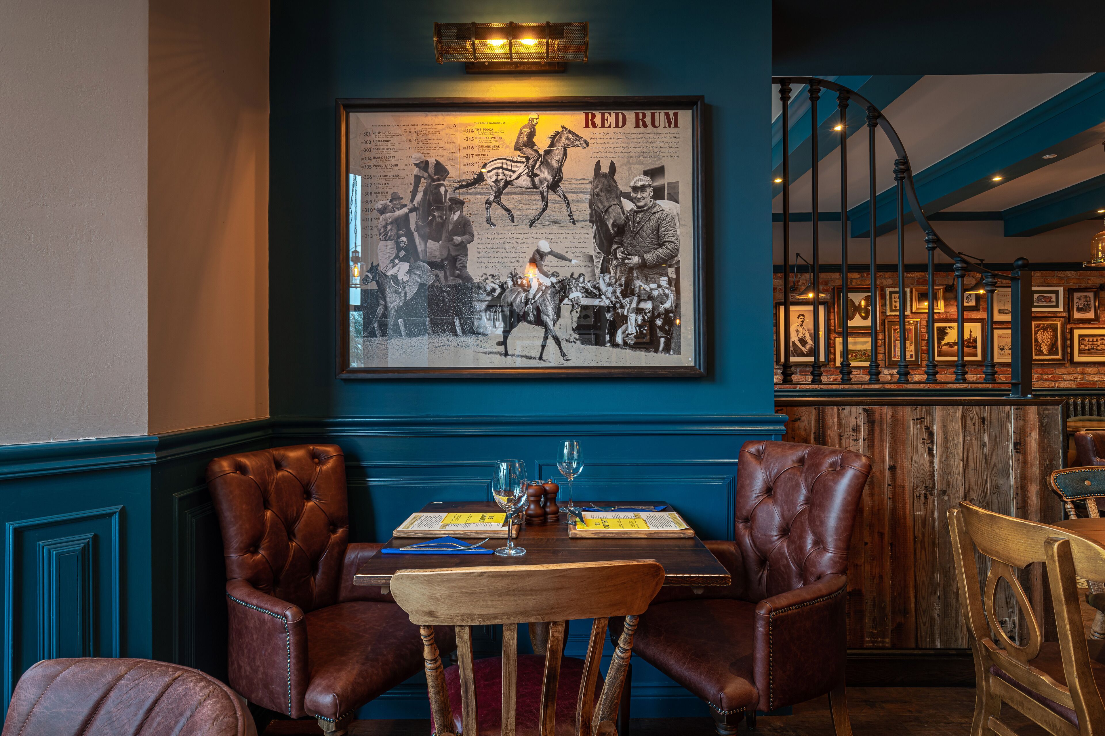 A restaurant interior with a framed historical poster, leather chairs, wooden tables, and a staircase.