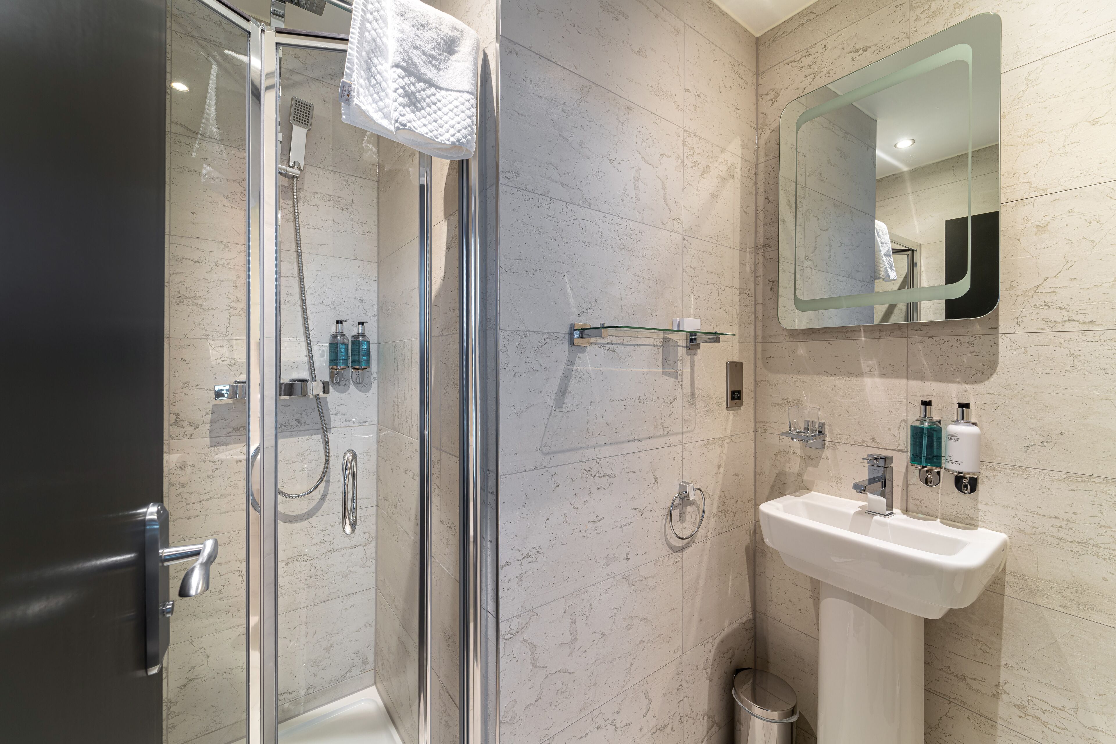 Ein modernes Badezimmer mit einer gläsernen Dusche, einem weißen Waschbecken und einem großen Spiegel.