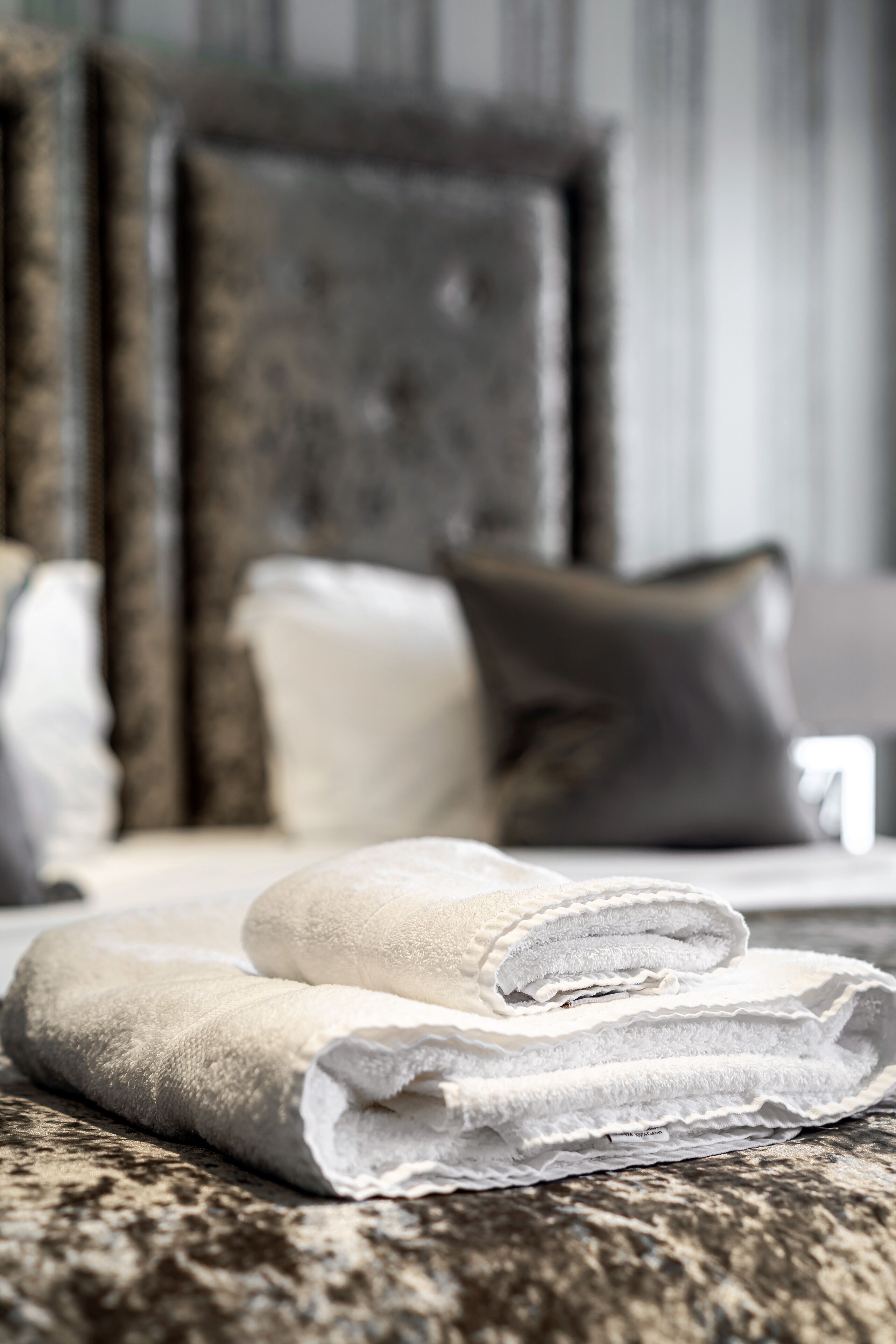 A neatly made bed with folded white towels and a dark headboard.