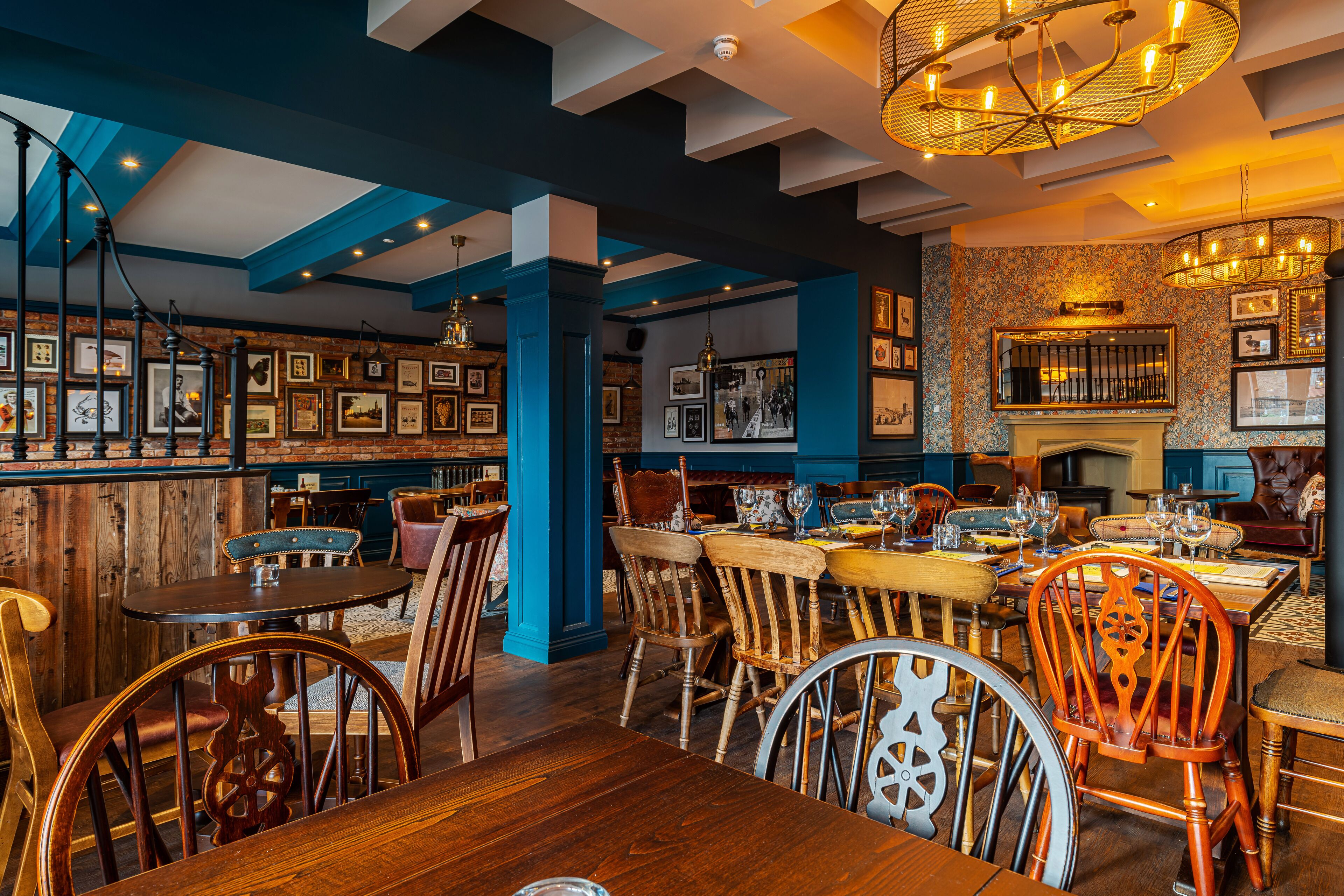 A restaurant interior with wooden tables and chairs, framed pictures on the walls, and a blue ceiling.