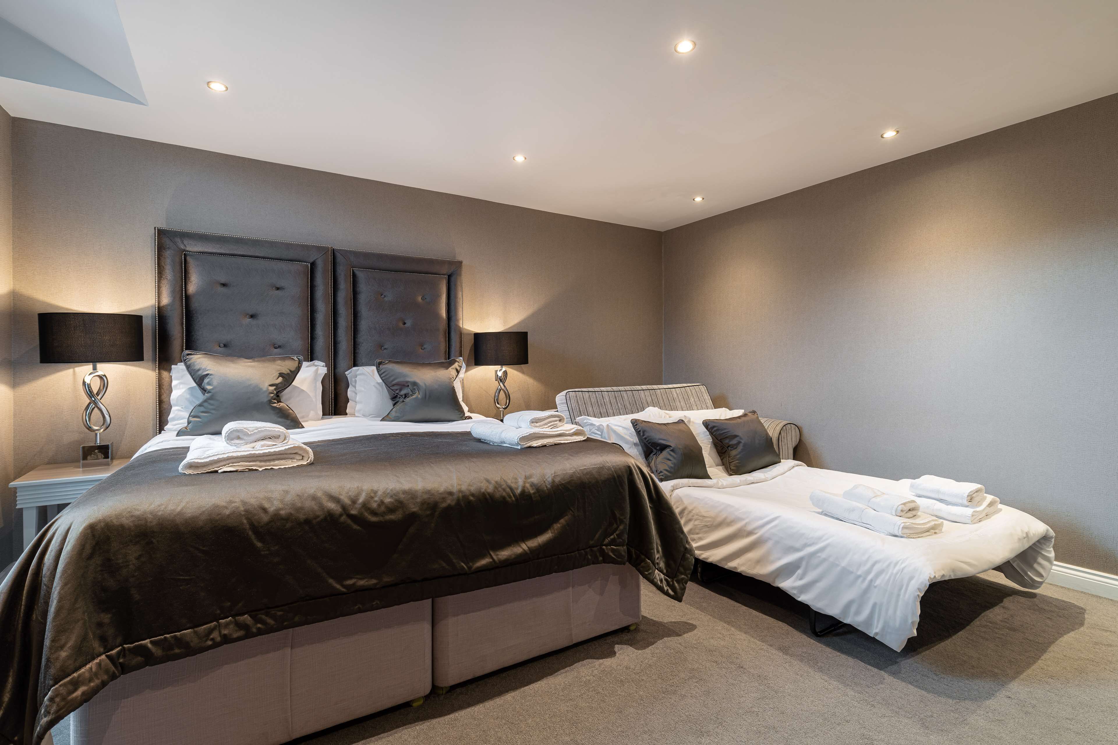 Habitación de hotel con dos camas, un cabecero grande y una mesita de noche con lámpara.