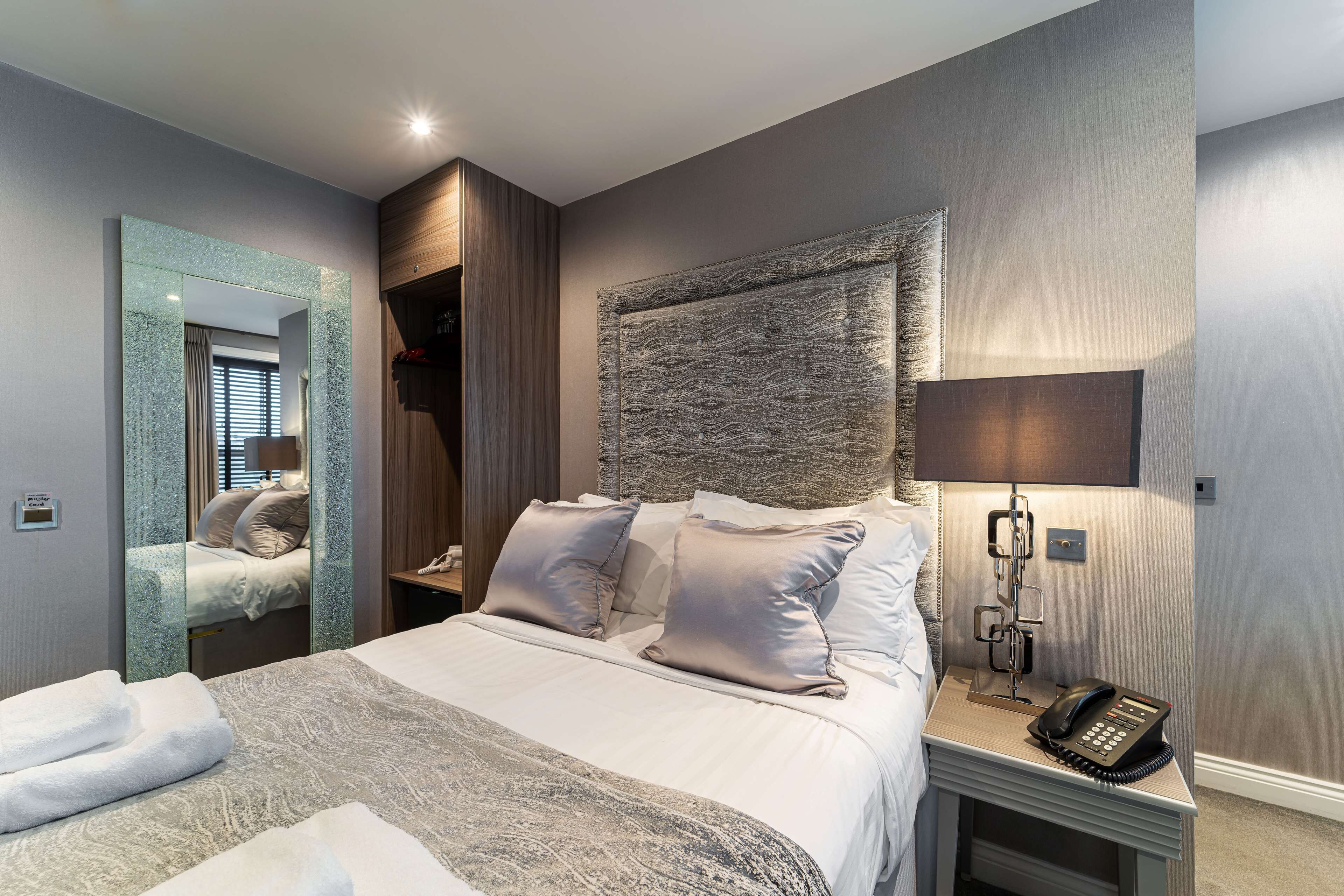 A modern hotel room with a large bed, a bedside telephone, and a mirror.